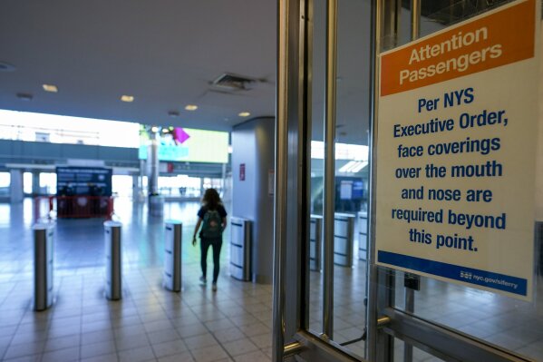 A sign advising passengers that face masks are required hangs on the entrance to the Staten Island ferry waiting room as a commuter runs to catch the ferry, Tuesday, Nov. 10, 2020, in New York. New York City officials are raising awareness and its efforts in stemming a rise in COVID-19 on Staten Island. (AP Photo/Mary Altaffer)