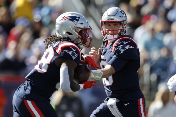New England Patriots quarterback Mac Jones, right, hands off to running back Rhamondre Stevenson, left, during the first half of an NFL football game against the New Orleans Saints, Sunday, Oct. 8, 2023, in Foxborough, Mass. (AP Photo/Michael Dwyer)