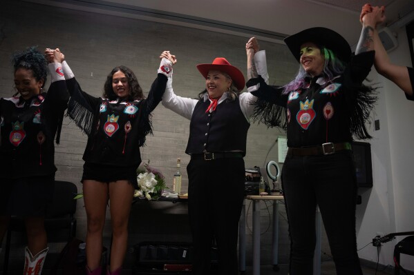 Mexican singer Vivir Quintana, center, and band members join hands before the introduction of her new album “Cosas que Sorprenden a la Audiencia” or Things that Surprise the Audience, in Mexico City, Thursday, April 24, 2025. Quintana's first "corridos" album tells the stories of women who were incarcerated for killing their abusers while defending themselves. (AP Photo/Aurea Del Rosario)