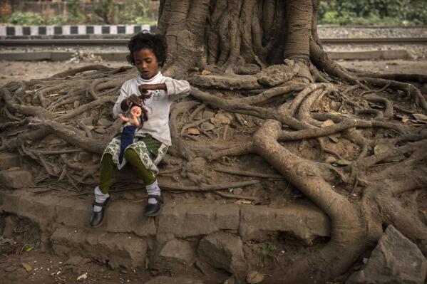A girl child plays with a doll sitting under a tree at a roadside, in Guwahati, in Indian northeastern state of Assam, Friday, Feb. 10, 2023. In India, the legal marriageable age is 21 for men and 18 for women. Poverty, lack of education, and social norms and practices, particularly in rural areas, are considered reasons for child marriages across the country. UNICEF estimates that at least 1.5 million girls under 18 get married in India every year, making it home to the largest number of child brides in the world, accounting for a third of the global total. (AP Photo/Anupam Nath)