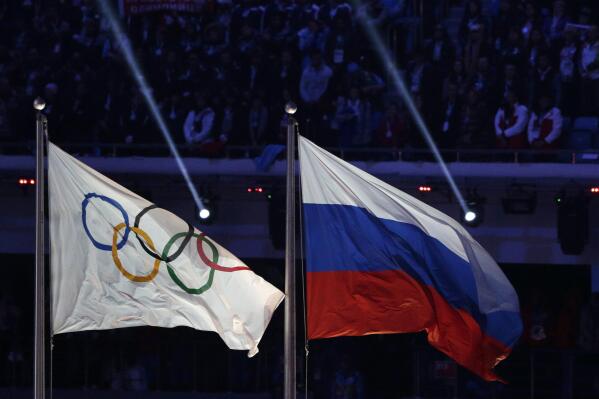 FILE - The Russian national flag, right, flies after it is hoisted next to the Olympic flag during the closing ceremony of the 2014 Winter Olympics in Sochi, Russia on Feb. 23, 2014. The International Olympic Committee has made a sweeping move to isolate and condemn Russia over the country’s invasion of Ukraine. (AP Photo/Matthias Schrader, File)