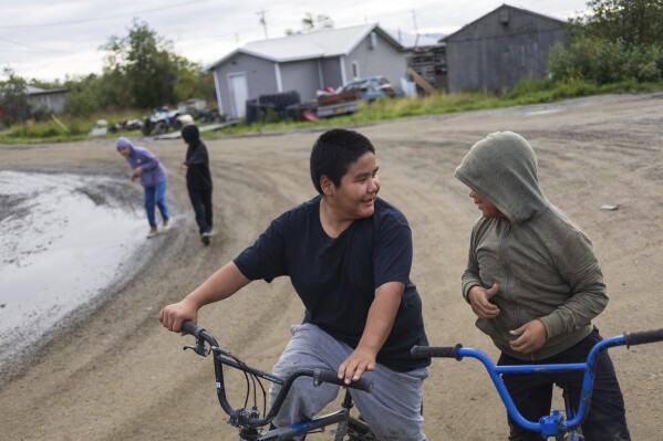 Maverick Chailes, 12, speaks to a friend while riding bikes, Friday, Aug. 18, 2023, in Akiachak, Alaska. (AP Photo/Tom Brenner)