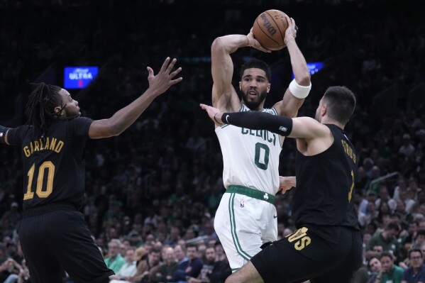 Boston Celtics forward Jayson Tatum (0) looks to pass while covered by Cleveland Cavaliers' Max Strus, right, and Darius Garland (10) during the first half of Game 1 of an NBA basketball second-round playoff series Tuesday, May 7, 2024, in Boston. (AP Photo/Charles Krupa)