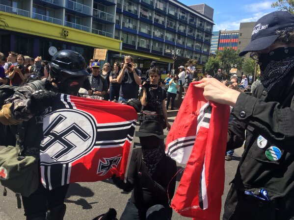 
              FILE - In this Aug. 4, 2018, file photo, counter protesters tear a Nazi flag, in Portland, Ore. A member of Portland's city council says she is shocked by a newspaper report that the commander for the police rapid response team exchanged friendly text messages with a leader of far-right protests that have rocked the city. Councilwoman Jo Ann Hardesty said the reporting in Willamette Week on Thursday, Feb. 14, 2019, confirms there are members of the Portland police force who work in collusion with right-wing extremists. (AP Photo/Manuel Valdes, File)
            