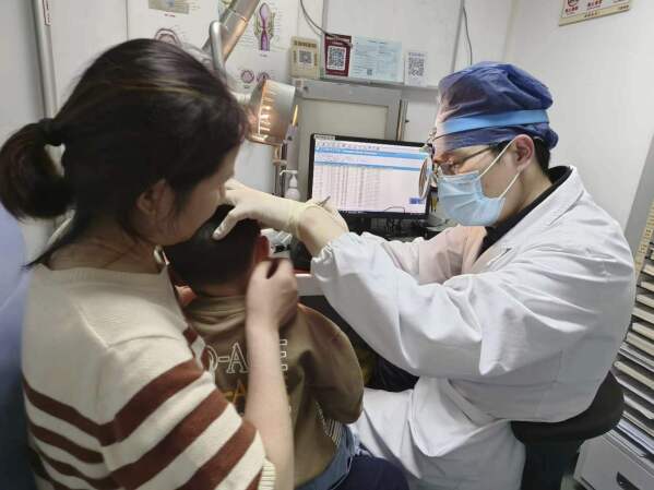 In this photo provided by researchers in January 2024, Dr. Yilai Shu examines a young patient at the Eye & ENT Hospital of Fudan University in Shanghai, China, after a gene therapy procedure for hereditary deafness. A small study published Wednesday, Jan. 25, 2024, in the journal Lancet, documents significantly restored hearing in five of six kids treated in China. (Courtesy Dr. Yilai Shu via AP)