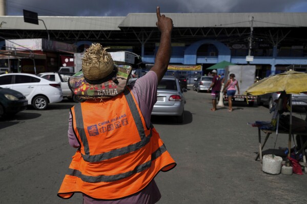 A car attendant wears a vest from the Chinese construction company Jinjiang, in the parking lot of the Municipal Market in Camacari, Bahia state, Brazil, Saturday, March 8, 2025. (AP Photo/Eraldo Peres)