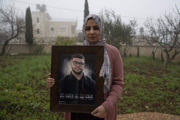 Mona, 36, mother of 17-year-old Tawfic Abdel Jabbar, a teenager from Louisiana who was fatally shot last week, poses with a framed photo underlain by the name of her son at the family's Palestinian home village in Al-Mazra'a ash-Sharqiya, West Bank, Tuesday, Jan. 23. (AP Photo/Nasser Nasser)