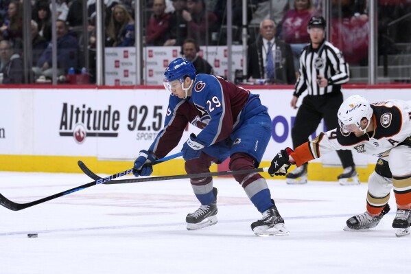 Colorado Avalanche center Nathan MacKinnon, left, reaches out to collect the puck as Anaheim Ducks defenseman Cam Fowler pursues during the first period of an NHL hockey game Tuesday, Dec. 5, 2023, in Denver. (AP Photo/David Zalubowski)