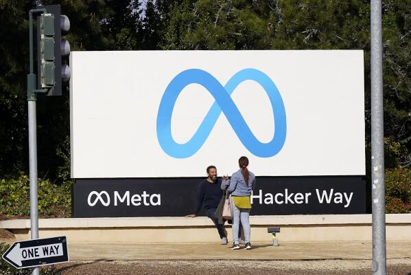 People talk near a Meta sign outside of the company's headquarters in Menlo Park, Calif., Tuesday, March 7, 2023. Facebook’s parent Meta will slash another 10,000 jobs and will not fill 5,000 open positions as the social media pioneer cuts costs. (AP Photo/Jeff Chiu)