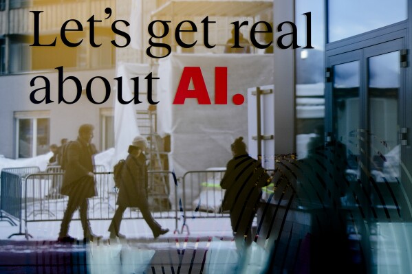 People reflected in a window of a hotel at the Davos Promenade with a slogan about AI alongside the World Economic Forum in Davos, Switzerland, Monday, Jan. 15, 2024. The AI technology has taken a large and growing slice of attention in Davos, this year the theme of Artificial Intelligence 
