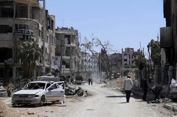 FILE - Syrians walk through destruction in the town of Douma, the site of a suspected chemical weapons attack, near Damascus, Syria, on April 16, 2018. The annual meeting of member states of the global chemical weapons watchdog on Thursday, Nov. 30, 2023 called on countries to prevent the sale or transfer to Syria of raw materials and equipment that could be used to create poison gas and nerve agents. (AP Photo/Hassan Ammar, File)