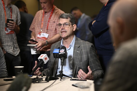 FILE - Los Angeles Chargers head coach Jim Harbaugh, center, talks with reporters during an AFC coaches availability at the NFL football owners meetings, Monday, March 25, 2024, in Orlando, Fla. Michigan was given three years of probation, fined and hit with recruiting limits by the NCAA on Tuesday, April 16, after football coaches and staff had impermissible contact with recruits and players under coach Jim Harbaugh while access was restricted during the COVID-19 pandemic.(AP Photo/Phelan M. Ebenhack, File)