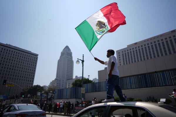 A protester waves a Mexico national flag  on top of a car near the metropolitan detention center, Monday, June 9, 2025, in downtown Los Angeles. (AP Photo/Eric Thayer)