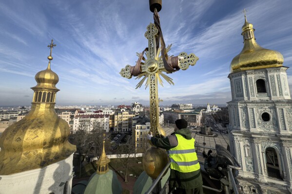Ihor Kuzmenko, altitude worker installs a restored cross on a dome of Saint Sophia Cathedral in Kyiv, Ukraine, Thursday, Dec. 21, 2023. A UNESCO World Heritage site, the gold-domed St. Sophia Cathedral, located in the heart of Kyiv, was built in the 11th century and designed to rival the Hagia Sophia in Istanbul. The monument to Byzantine art contains the biggest collection of mosaics and frescoes from that period, and is surrounded by monastic buildings dating back to the 17th century. (AP Photo/Evgeniy Maloletka)