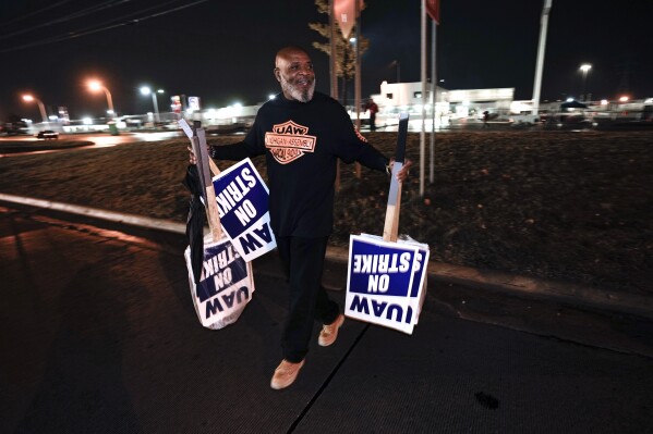 United Auto Workers member Marcel Edwards carries On Strike signs from the picket line to Local 900 headquarters at the Ford Michigan Assembly Plant in Wayne, Mich., Wednesday, Oct. 25, 2023. The United Auto Workers union said Wednesday it has reached a tentative contract agreement with Ford that could be a breakthrough toward ending the nearly 6-week-old strikes against Detroit automakers. (AP Photo/Paul Sancya)