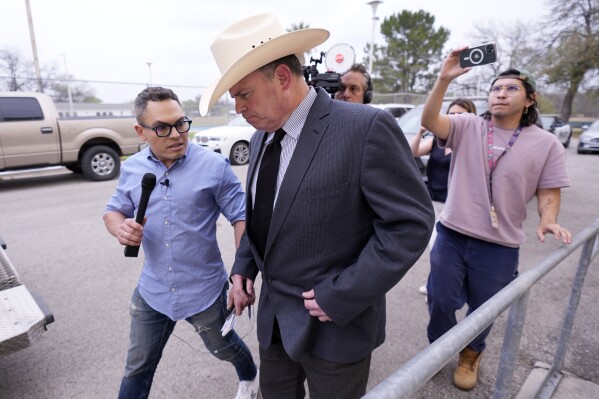Jesse Prado, center in cowboy hat, an Austin-based investigator, is pursued by the media after he shared his findings at a special city council meeting in Uvalde, Texas, Thursday, March 7, 2024. (AP Photo/Eric Gay)
