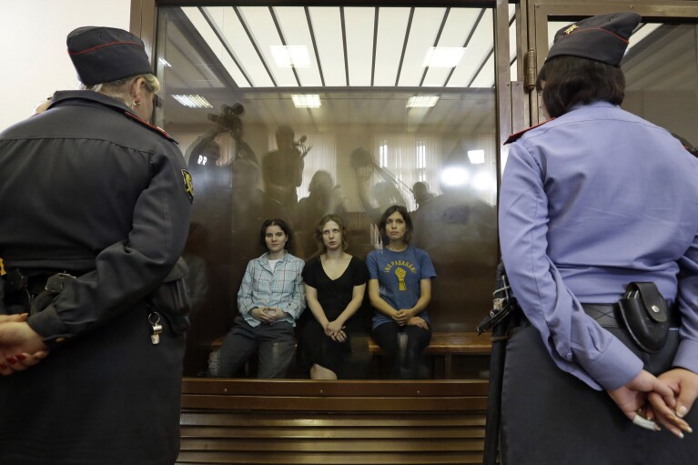 FILE - Feminist punk group Pussy Riot members, from left, Yekaterina Samutsevich, Maria Alekhina and Nadezhda Tolokonnikova sit in a defendants’ cage at a court in Moscow, Russia, Aug. 17, 2012. Over the last decade, Vladimir Putin's Russia evolved from a country that tolerates at least some dissent to one that ruthlessly suppresses it. Arrests, trials and long prison terms — once rare — are commonplace. (AP Photo, File)