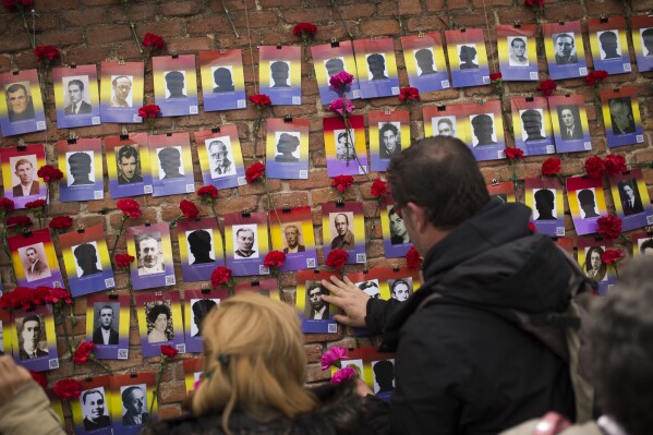 FILE - People put red carnations next to photographs during the 87th Spanish Republic anniversary ceremony to pay tribute to people killed in the Spanish Civil War at the Almudena cemetery in Madrid, on April 14, 2018. Spain’s Catalonia regional government says it has identified 357 foreign militiamen who disappeared in the region during the Spanish Civil War. Of these, 212 are Germany, Austria and Netherlands nationals. Researchers have also been able to find the likely exact area where all they died or were badly wounded. (AP Photo/Francisco Seco, File)