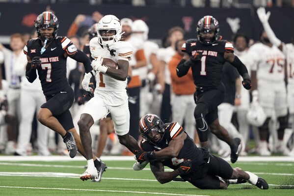 Texas wide receiver Xavier Worthy (1) is tackled after a long gain by Oklahoma State linebacker Nickolas Martin (4) as safety Cameron Epps (7) and linebacker Xavier Benson (1) follow behind in the first half of the Big 12 Conference championship NCAA college football game in Arlington, Texas, Saturday, Dec. 2, 2023. (AP Photo/Tony Gutierrez)
