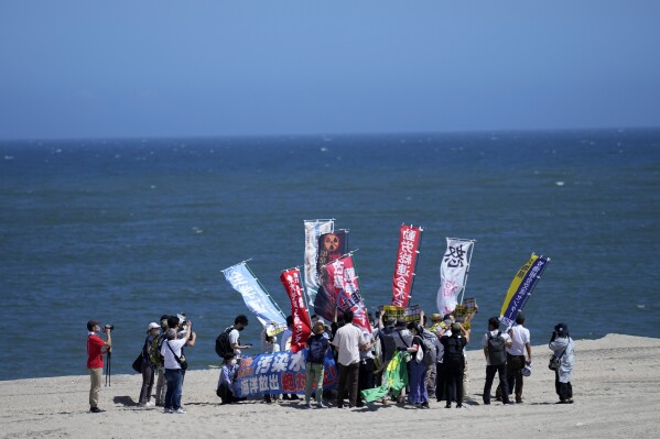 La gente protesta en una playa hacia la planta de energía nuclear de Fukushima Daiichi, dañada por un enorme terremoto y tsunami el 11 de marzo de 2011, en la ciudad de Namie, noreste de Japón, el jueves 24 de agosto de 2023. El operador de la Fukushima Daiichi destrozada por el tsunami La planta de energía nuclear dice que comenzó a liberar su primer lote de agua radiactiva tratada en el Océano Pacífico el jueves, un paso controvertido, pero un hito en la batalla de Japón contra las crecientes reservas de agua radiactiva.  (Foto AP/Eugene Hoshiko)