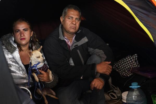 Hondurans Ana Morazan, left, holds her dog, Jabibi, as she and her boyfriend Fredi Juarez, sit in their tent inside a migrant shelter Friday, May 20, 2022, in the border city of Tijuana, Mexico. Back-to-back hurricanes destroyed her home in Honduras in 2020, forcing her and Juarez to join the millions of people uprooted by rising seas, drought, searing temperatures and other climate catastrophes. (AP Photo/Gregory Bull)