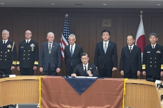 Japanese and U.S. military officials and U.S. Ambassador to Japan Rahm Emanuel, fourth left, and Japanese Defense Minister Minoru Kihara, third right, stand behind a defense equipment procurement official as he signs a document for the Tomahawk purchase deal at the Japanese Defense Ministry, in Tokyo, Thursday, Jan. 18, 2023. Japan has signed a deal with the United States to purchase up to 400 Tomahawk cruise missiles as part of its ongoing military buildup in response to increased regional threats. U.S. Ambassador to Japan Rahm Emanuel attended a signing event at Japan's Defense Ministry on Thursday. (AP Photo/Mari Yamaguchi)