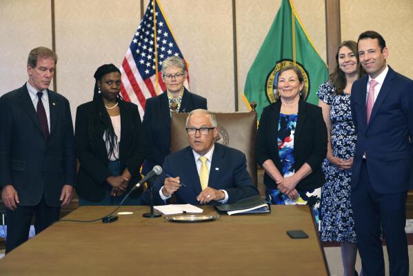 Gov. Jay Inslee signs Senate Bill 5536 concerning controlled substances on Tuesday, May 16, 2023, in Olympia, Wash. Behind him are from left to right: Rep. Roger Goodman, D- Kirkland, Rep. Jamila Taylor, D-Federal Way, House Speaker Laurie Jinkins, D-Tacoma, June Robinson, D-Everett, an identified woman and Andy Billig, D-Spokane. The policy, approved by Washinton lawmakers and signed by Inslee, keeps controlled substances illegal while boosting resources to help those struggling with addiction. (Karen Ducey/The Seattle Times via AP)