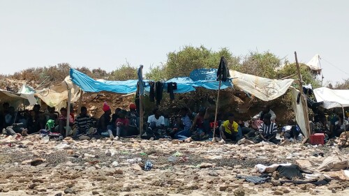 In this photo taken by 29-year-old migrant from the Ivory Coast, a group of sub-Saharan Africans is seen stranded on a beach allegedly at the Tunisian-Libyan border on Thursday 6 July 2023. The migrants, including women and small children, told AP by phone they were rounded up by Tunisian authorities since Saturday and progressively dumped on the border where they have been stuck for days. (UGC via AP)