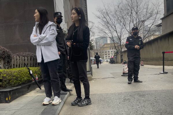 Women stand near security personnel outside the barricaded Sichuan Trust office building in Chengdu in southwestern China's Sichuan Province on Feb. 27, 2024. Some investors in a troubled trust fund in China are facing financial ruin under a government plan to return a fraction of their money, casualties of a slump in the property industry and a broader economic slowdown. (AP Photo/Andy Wong)