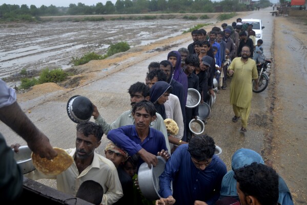 People wait for their turn to receive free food distributed by volunteers outside a camp for internally displaced people from coastal areas, as Cyclone Biparjoy was approaching, in Sujawal, Pakistan's southern district in the Sindh province, Thursday, June 15, 2023. A vast swath of western India and neighboring southern Pakistan that suffered deadly floods last year are bracing for a new deluge as fast-approaching Cyclone Biparjoy whirls toward landfall Thursday. (AP Photo/Pervez Masih)