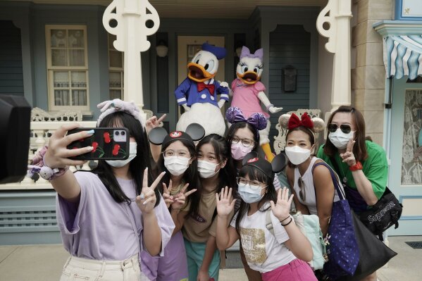 Visitors wearing face masks take a selfie with the iconic cartoon characters Donald Duck and Daisy Duck at the Hong Kong Disneyland, Friday, Sept. 25, 2020. Hong Kong Disneyland reopened its doors to visitors after closed temporarily due to the coronavirus outbreak. (AP Photo/Kin Cheung)