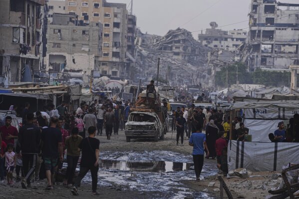 A damaged car carrying furniture and a mattress drives among pedestrians through a market surrounded by destroyed buildings in Gaza City, northern Gaza Strip, on Sunday, June 22, 2025. (AP Photo/Jehad Alshrafi)