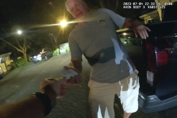 In this image from video provided by the Tampa Police Department, Joseph Ruddy, a prosecutor with the U.S. Attorney’s Office in Tampa, hands his business card to Officer Taylor Grant, outside his home in Temple Terrace, Fla., on the evening of July 4, 2023. When police arrived at his house to investigate a hit-and-run, Ruddy, one of the nation’s most prolific federal narcotics prosecutors, was so drunk he could barely stand up straight, leaning on the tailgate of his pickup to keep his balance. (Officer Taylor Grant/Tampa Police Department)
