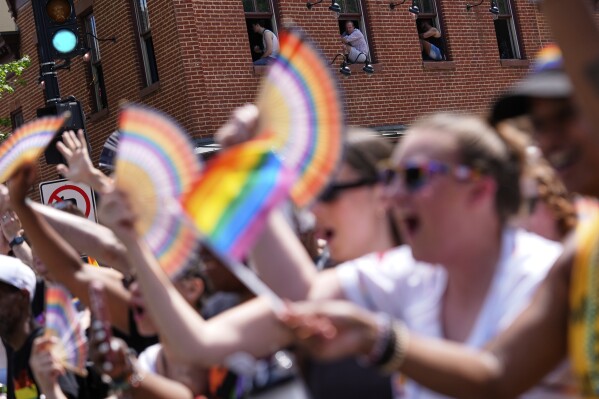 People sit in the windows sills of a building as the World Pride parade passes, Saturday, June 7, 2025, in Washington. (AP Photo/Julia Demaree Nikhinson)