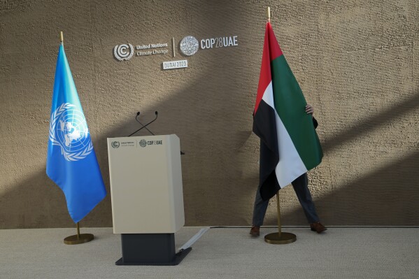 A person adjusts the flag of the United Arab Emirates ahead of a news conference by United Nations Climate Chief Simon Stiell at the COP28 U.N. Climate Summit, Dec. 11, 2023, in Dubai, United Arab Emirates. (AP Photo/Kamran Jebreili)