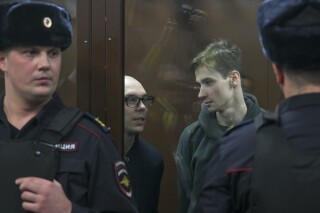 Artyom Kamardin, left, and Yegor Shtovba, right, stand behind a glass in a cage in a courtroom in Moscow, Russia, Thursday, Dec. 28, 2023. Artyom Kamardin was given a 7-year prison sentence Thursday for reciting verses against Russia's war in Ukraine, a tough punishment that comes during a relentless Kremlin crackdown on dissent. Yegor Shtovba, who participated in the event and recited Kamardin's verses, was sentenced to 5 1/2 years on the same charges. (AP Photo)