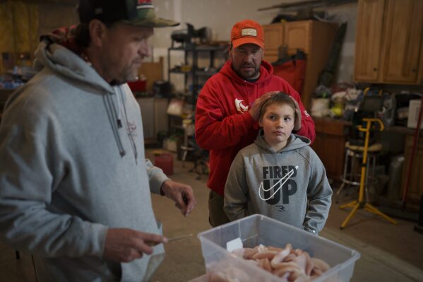 Kelly Martin, left, prepares fillets of walleye as Anthony Martin, center, and his son Caleb Ryan watch during a fish fry Friday, April 19, 2024, in Hayward, Wis. (AP Photo/John Locher)