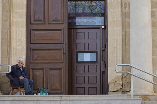A man sits outside St. George Church in the Maronite village of Kormakitis in the breakaway north of the ethnically divided Cyprus on Wednesday, April 23, 2025. (AP Photo/Petros Karadjias)