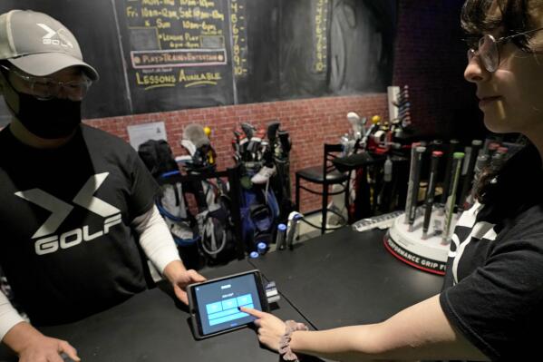 X-Golf manager J.W. Park, left, helps Ashley Moreno to check out at X-Golf indoor golf in Glenview, Ill., Friday, Jan. 20, 2023. Tipping fatigue, it seems, is swarming America as more businesses adopt digital payment methods that automatically prompts customers to leave a gratuity. (AP Photo/Nam Y. Huh)