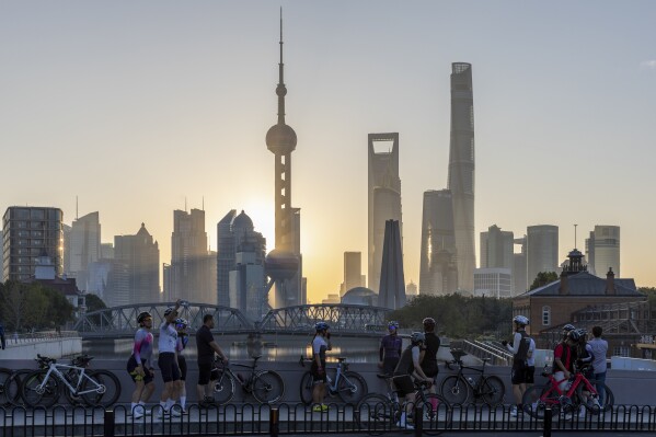 FILE - In this photo released by Xinhua News Agency, cyclists, some take selfie as they take rest against the sunrise skylines in Pudong, China's financial and commercial hub, in Shanghai, China on Friday, Nov. 3, 2023. Credit rating agency Moody’s cut its outlook for Chinese sovereign bonds to negative on Tuesday, Dec. 5, 2023, citing risks from a slowing economy and a crisis in its property sector.(Wang Xiang/Xinhua via AP, File)
