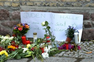 FILE -- In this Oct. 10, 2019 file photo, candles and flowers are placed in front of a synagogue in Halle, Germany after a heavily armed assailant ranting about Jews tried to force his way into the synagogue in Germany on Yom Kippur, Judaism's holiest day, then shot two people to death nearby in an attack.  Sign reads, "Jews in Halle - We stay next to you! You are not alone." Israeli researchers in their annual report released Monday, April 20, 2020, reported that the global outbreak of the coronavirus has sparked a rise in anti-Semitic expression blaming the Jews for the spread of the disease and the economic recession it has caused. (AP Photo/Jens Meyer, File),