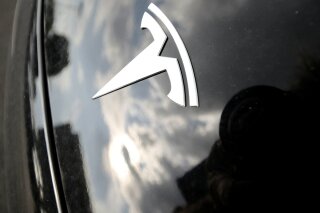 FILE - In this July 8, 2018, file photo, clouds are reflected above the company logo on the hood of a Tesla vehicle outside a showroom in Littleton, Colo. The National Highway Traffic Safety Administration is investigating the crash of a speeding Tesla that killed two people in a Los Angeles suburb, the agency announced Tuesday, Dec. 31, 2019. (AP Photo/David Zalubowski, File)