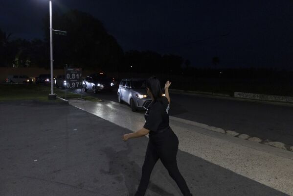 A gas station employee directs traffic as cars line up for fuel during an island-wide blackout in San Juan, Puerto Rico, Wednesday, April 16, 2025. (AP Photo/Alejandro Granadillo)