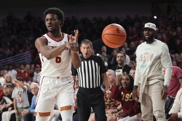 CORRECTS TO SECOND HALF NOT FIRST HALF - Southern California guard Bronny James, left, passes the ball as his father LeBron James, right, watches during the second half of an NCAA college basketball game against Long Beach State, Sunday, Dec. 10, 2023, in Los Angeles. (AP Photo/Mark J. Terrill)