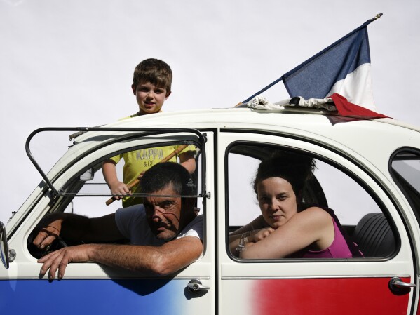 Philippe Planet poses for a portrait with his daughter Laurine and grandson Evan Bousset in their tricolour Citroen 2CV during the tenth stage of the Tour de France cycling race over 167 kilometers (104 miles) with start in Vulcania and finish in Issoire, France, Tuesday, July 11, 2023. (AP Photo/Daniel Cole)