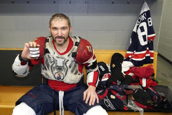Washington Capitals' Alex Ovechkin holds his 798, 799, and 800th career goal pucks in the locker room next to hats collected for his hat trick after an NHL hockey game against the Chicago Blackhawks Tuesday, Dec. 13, 2022, in Chicago. (AP Photo/Charles Rex Arbogast)