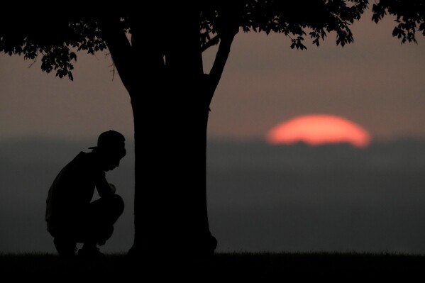 FILE - A boy rests under a tree while watching the sun set as triple-digit heat indexes continue in the Midwest, Aug. 20, 2023, in Kansas City, Mo. (AP Photo/Charlie Riedel, File)