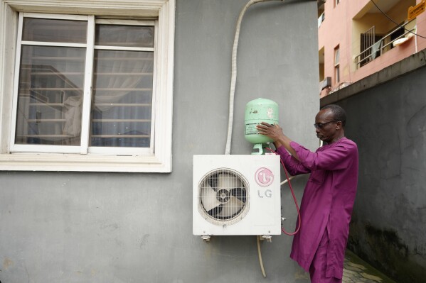 A technician positions an R-22 refrigerant on an outdoor air conditioning unit in Lagos, Nigeria, Thursday, July 18, 2024. (ĢӰԺ Photo/Sunday Alamba)