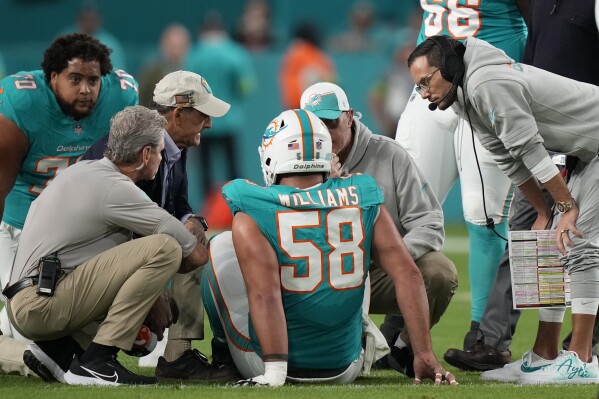 Miami Dolphins head coach Mike McDaniel, right, checks on guard Connor Williams (58) as he is attended on the field during the first half of an NFL football game against the Tennessee Titans, Monday, Dec. 11, 2023, in Miami, Fla. (AP Photo/Lynne Sladky)