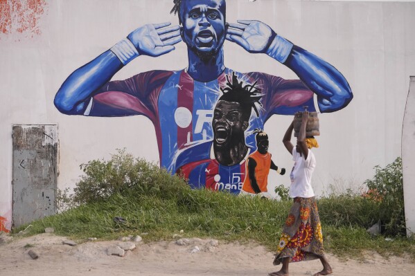 A woman walks past a portrait of Ivory Coast Soccer player Wilfried Zaha on the street in Abidjan, Ivory Coast, Monday, Feb. 5, 2024. (APPhoto/Sunday Alamba)